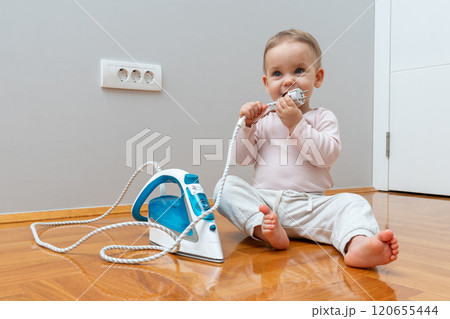 A baby exploring an iron cord while sitting on the floor near an electrical outlet, emphasizing the need for safety and caution. A baby exploring an iron cord while sitting on the floor near an electrical outlet, emphasizing the need for safety and caution. 120655444