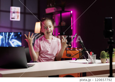 Smiling girl filming room tour inside home studio using cellphone on tripod stabilizer. Young internet star doing video presenting apartment to interested children audiences 120657792