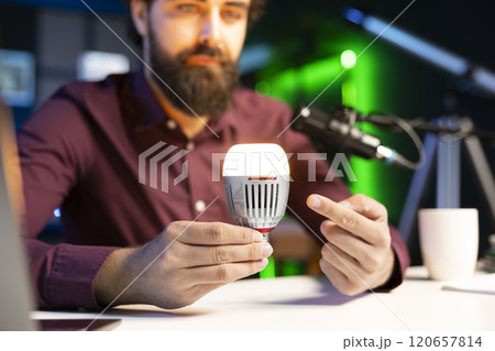 Close up shot of smart light bulb used by tech guru to teach viewers how to do maintenance. Focus on IoT home automation product held by content creator in blurry background 120657814
