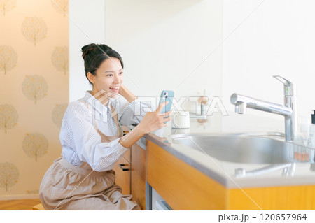 キッチンでスマホを見る女性 120657964
