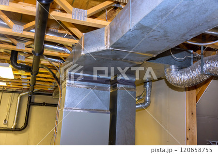 Metal ductwork is residential basement, displaying well organized HVAC system installation features various pipes, vents overhead, ensuring proper air circulation. Metal ductwork is residential basement, displaying well organized HVAC system installation features various pipes, vents overhead, ensuring proper air circulation. 120658755