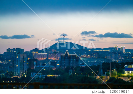 Evening city in pink sunset with flag on mountain. 120659014