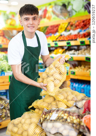 Young male seller laying out and offering bag of potatoes in grocery store 120659237