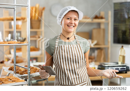 Portrait of cheerful baker girl with knife cutting raw dough in kitchen of private bakery 120659262