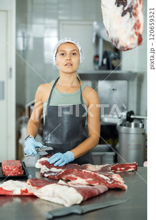 Girl in butcher shop cuts meat carcass into small pieces of meat for retail sale in small store 120659321