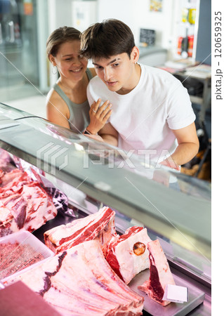 Spouse near butcher shop window inspects goods and choose piece of beef for cooking rib eye steak Spouse near butcher shop window inspects goods and choose piece of beef for cooking rib eye steak 120659325