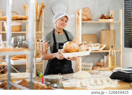 Young woman baker are standing near product range in bakery kitchen with basket of bread. Young woman baker are standing near product range in bakery kitchen with basket of bread. 120659425