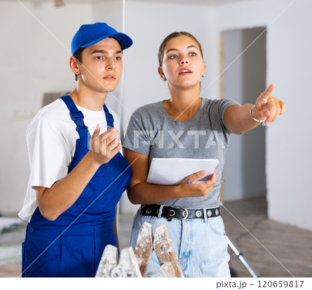 Female designer with papers talking to contractor in building during renovation 120659817