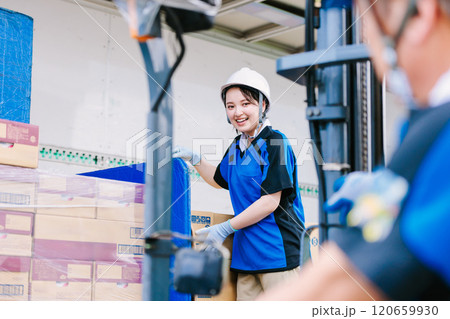 トラックにフォークリフトで荷物を積むヘルメット姿の女性作業員 120659930