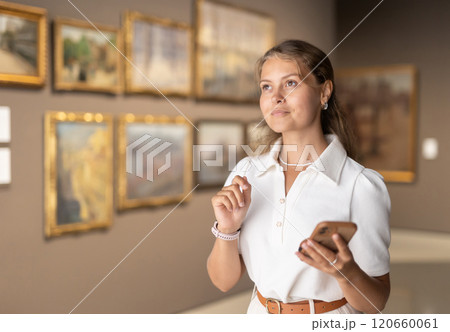 Woman with phone in hands view pictures and icons in museum hall Woman with phone in hands view pictures and icons in museum hall 120660061