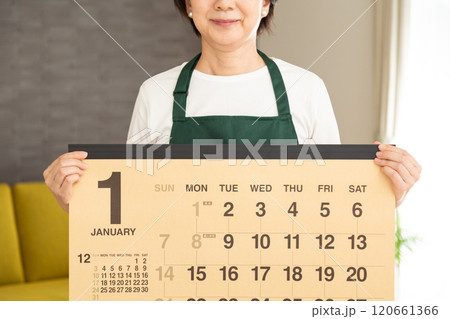 家のリビングでカレンダーを持つ緑のエプロンをしたミドル〜シニア女性の主婦 家のリビングでカレンダーを持つ緑のエプロンをしたミドル〜シニア女性の主婦 120661366