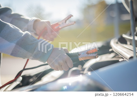 Woman holding clamps for charging a car battery. Woman holding clamps for charging a car battery. 120664254
