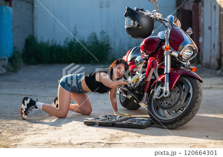 Brunette woman in denim shorts repairs a red motorcycle.  120664301