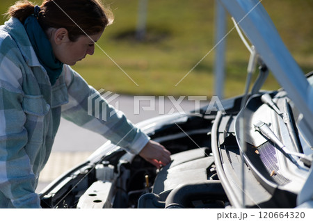 Caucasian female driver checking oil level in car engine. Caucasian female driver checking oil level in car engine. 120664320