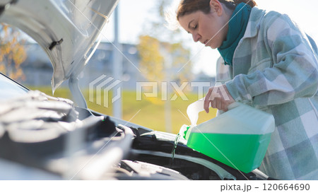 Caucasian woman filling car reservoir with windshield washer fluid from bottle. Caucasian woman filling car reservoir with windshield washer fluid from bottle. 120664690