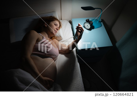 A pregnant woman lies in bed and uses a smartphone. Insomnia. 120664821