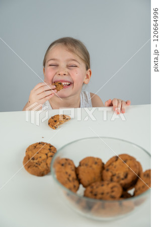 A little girl steals cookies from the table. Vertical photo.  120664996