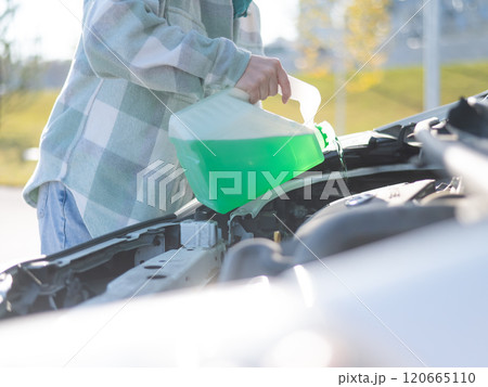Close up of female hands filling car reservoir with windshield washer fluid from bottle. Close up of female hands filling car reservoir with windshield washer fluid from bottle. 120665110