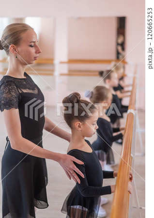 Caucasian woman teaches little girls ballet at the barre. Vertical photo. Caucasian woman teaches little girls ballet at the barre. Vertical photo. 120665253