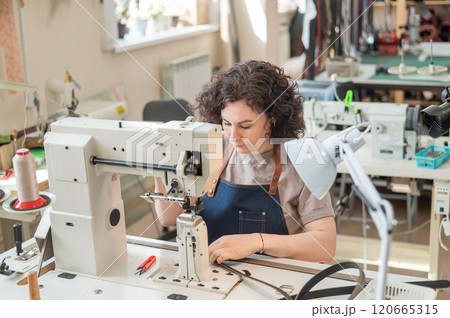 A woman tanner sews a leather belt on a sewing machine.  120665315