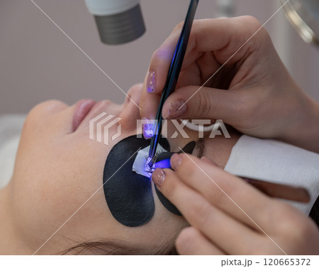 A woman undergoing eyelash extension procedure using an ultraviolet lamp. 120665372