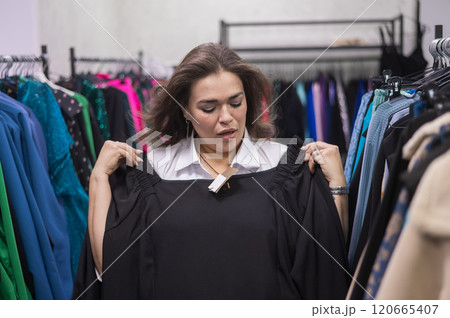 A fat woman in a plus size store tries on a black evening dress. Vertical photo. A fat woman in a plus size store tries on a black evening dress. Vertical photo. 120665407