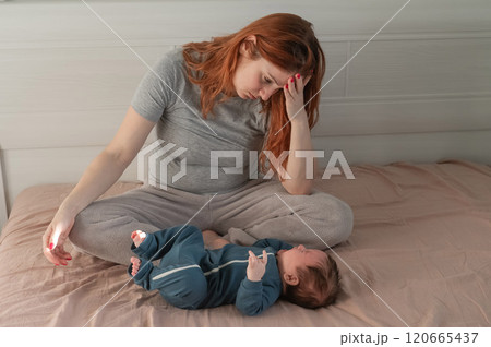 A Caucasian woman sits on a bed next to a crying baby. Postpartum depression. 120665437