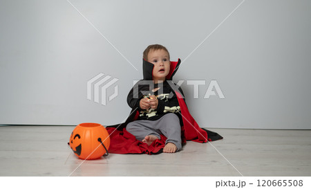 Little Caucasian boy in Dracula costume holding skull on white background.  120665508