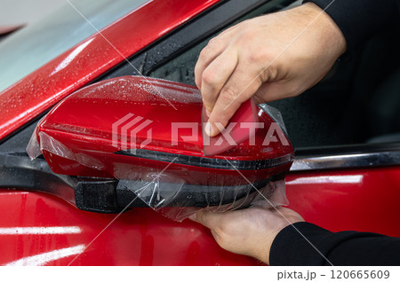 The master applies vinyl film to the side view mirror of a car. The master applies vinyl film to the side view mirror of a car. 120665609
