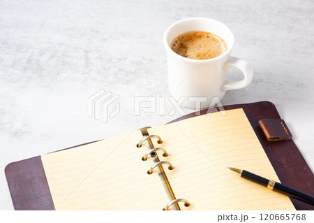 ミルクを入れたコーヒー、カフェ・ラッテを飲みながら、茶色の革のシステム手帳でデスクワーク中のイメージ ミルクを入れたコーヒー、カフェ・ラッテを飲みながら、茶色の革のシステム手帳でデスクワーク中のイメージ 120665768