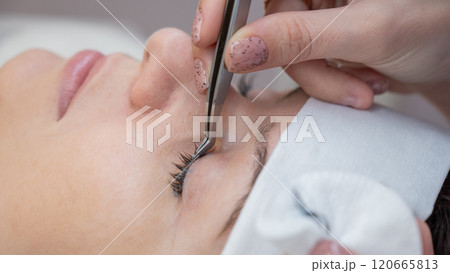 A master removes eyelash extensions from a client. 120665813