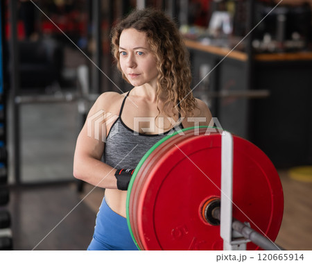 Caucasian forty year old woman putting a weight plate on a barbell in the gym.  120665914