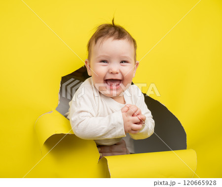 Cheerful baby rips and sticks out through yellow cardboard background. Cheerful baby rips and sticks out through yellow cardboard background. 120665928