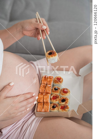 A pregnant woman sits on the sofa and eats rolls from a box. Food delivery. Close up of belly.  120666120