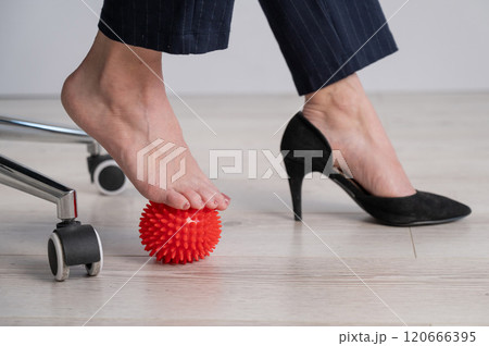 Business woman massages her feet on a massage ball with spikes. 120666395