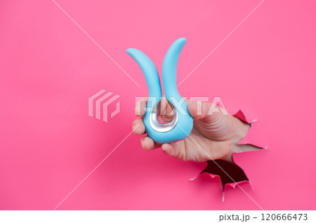Female hand sticking out of pink paper background with blue curved vibrator sex toy.  120666473