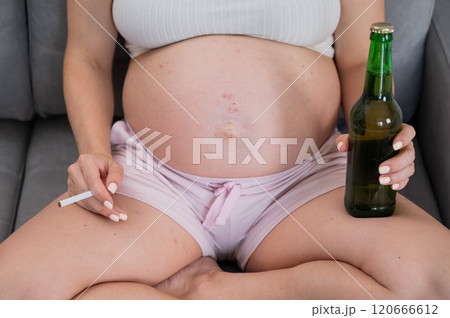 Faceless pregnant woman drinks beer while sitting on the sofa.  120666612