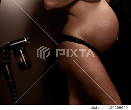 Faceless pregnant woman getting an instant tan. The master applies bronzer with a spray. 120666640