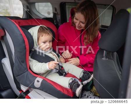 Caucasian woman buckles her toddler son into a car seat. Caucasian woman buckles her toddler son into a car seat. 120666645