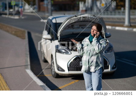 Caucasian woman calls on the phone and asks for help while standing near a car with an open hood. Caucasian woman calls on the phone and asks for help while standing near a car with an open hood. 120666801