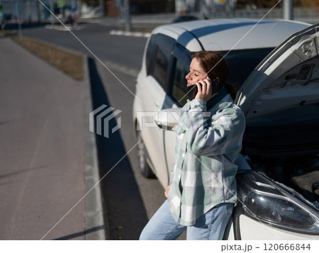 Sad Caucasian woman calling on phone while standing near car with open hood.  120666844