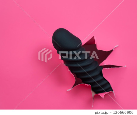 Black ribbed dildo sticking out of hole on pink background. Black ribbed dildo sticking out of hole on pink background. 120666906