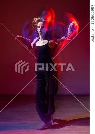 A young woman dances contemporary dances in blue and red light. Long exposure. Vertical photo.  120666997