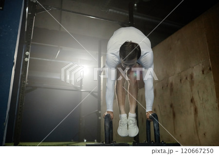 Low angle shot of professional male athlete taking off to press into handstand balancing on parallettes practicing calisthenics against backlight in gym, copy space 120667250