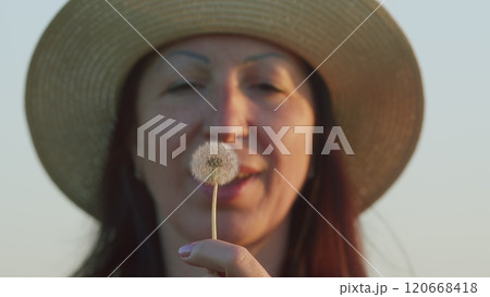 Brunette Woman In A Dress Enjoying Summer In Countryside At Sunset. Beautiful Young Woman In A Field Blow Dandelion. Close Up. Brunette Woman In A Dress Enjoying Summer In Countryside At Sunset. Beautiful Young Woman In A Field Blow Dandelion. Close Up. 120668418