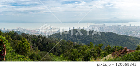 Panoramic view of GeorgeTown cityscape in Malaysia from hilltop with lush green forest foreground, high-rise buildings, calm sea, cloudy sky, showcasing blend urban natural beauty, scenic skyline 120669843