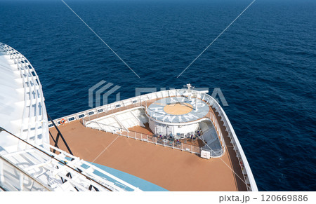 Aerial view of cruise ship, showcasing top deck with swimming pools, sun loungers, sailing in clear blue ocean waters 120669886
