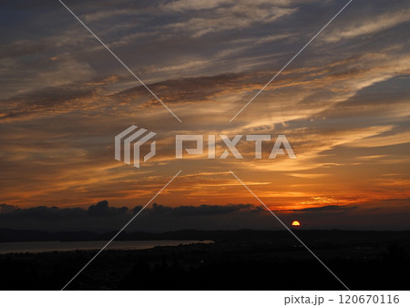 雲に沈む夕日とオレンジ色に輝く雲が暗い青空に印象的で綺麗だ。 雲に沈む夕日とオレンジ色に輝く雲が暗い青空に印象的で綺麗だ。 120670116