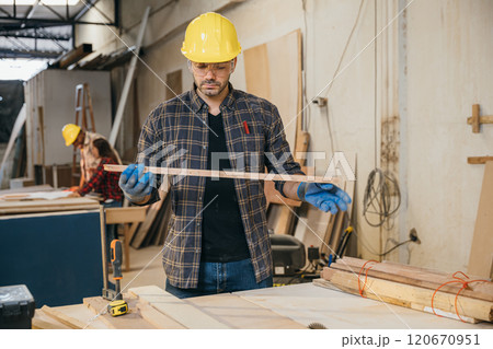 Carpenter man holding piece of wood surrounded by other wood pieces, showcasing craftsmanship and happiness at work in a furniture factory. Ideal for woodworking and craftsmanship concepts. Labor day 120670951