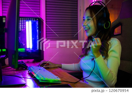 Winning Victory. Asian gamer playing online video game excited on desktop computer PC colorful neon LED lights, woman in gaming headphones use computer she happy successful, E-Sport concept, side view Winning Victory. Asian gamer playing online video game excited on desktop computer PC colorful neon LED lights, woman in gaming headphones use computer she happy successful, E-Sport concept, side view 120670954